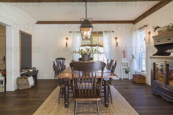 Brown stained pine wood antique reproduction style dining table with high back chairs in dining room with rug and dark brown larch wood floorboards inside country style home, Quebec, Canada, North America