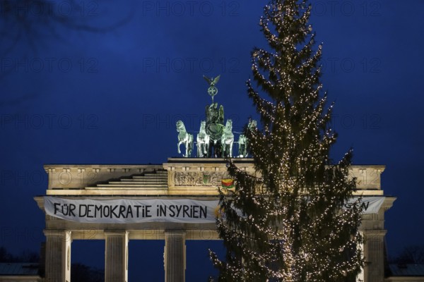 A banner For Democracy in Syria / Defend Rojava hangs behind a Christmas tree at the Brandenburg Tor, Berlin, 16 December 2024