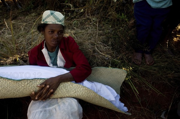 Young woman participating in a famadihana. This funerary tradition is also known as the turning of the dead. At this time, the descendants of the deceased open the family grave, rewrap the bodies with new white shroud and dance with the bodies. On this photo, the woman is seen holding the body of one of her ancestors. Near Ambositra, Madagascar. This tradition is followed by the Betsileo ethnic group