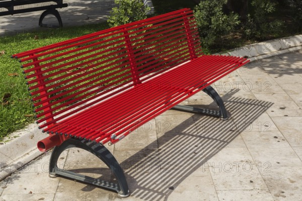 Red painted sitting bench with seat and backrest made of round metal tubes on the grounds of the Zanca Palace or the Messina Town Hall building in late summer, Messina, Sicily, Italy, Europe