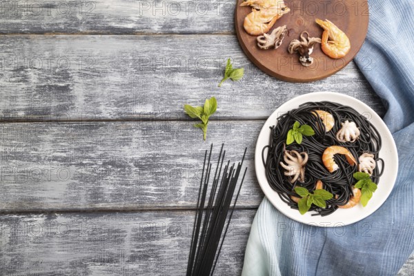 Black cuttlefish ink pasta with shrimps or prawns and small octopuses on gray wooden background and blue textile. Top view, flat lay, copy space