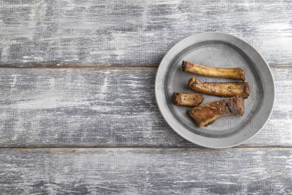 Pork ribs on a wooden plate on a gray wooden background. Top view, flat lay, close up, copy space