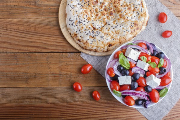 Greek salad with fresh cherry tomatoes, feta cheese, black olives, basil and onion on wooden background, pancake, top view, copy space