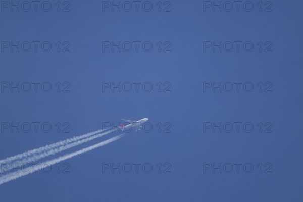 Boeing 747 jumbo jet aircraft flying across a blue sky with a vapour trail or contrail behind, England, United Kingdom, Europe