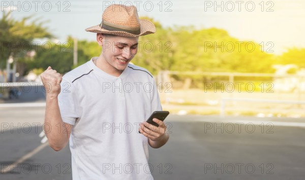 Man with winning gesture using cell phone in the street. Happy young man with winning gesture with cellphone on the street