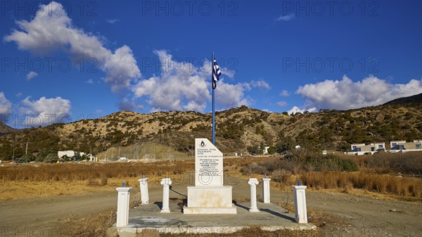 Monument with Greek flag in front of a clear blue sky and mountain landscape in the background, Christopher Litos Monument, Pigadia, town and harbour, Pigadia Bay, main town, Karpathos, Dodecanese, Greek Islands, Greece, Europe