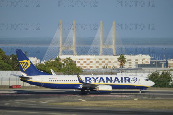 Lisbon, Portugal - September 2, 2023: Ryanair Boeing 737-8AS passenger plane taxi on runway in Humberto Delgado Airport in Lisbon with Vasco da Gamma bridge in background