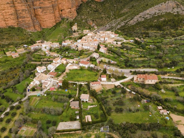 Aerial view of a picturesque village surrounded by green hills and striking orange rocks, aerial view, Las Peñas de Riglos, As Penyas de Riglos, Mallos de Riglos rock formation, Huesca, Aragon, Spain, Europe