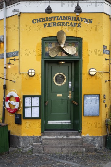 Green entrance door with ship's propeller, yellow painted façade, Christianshavns Færgecafé, Wilders Canal, Copenhagen, Denmark, Europe