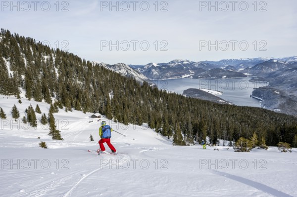 Skiers skiing down the Simetsberg, view of Walchensee and mountain panorama, Estergebirge, Bavarian Prealps, Bavaria Germany