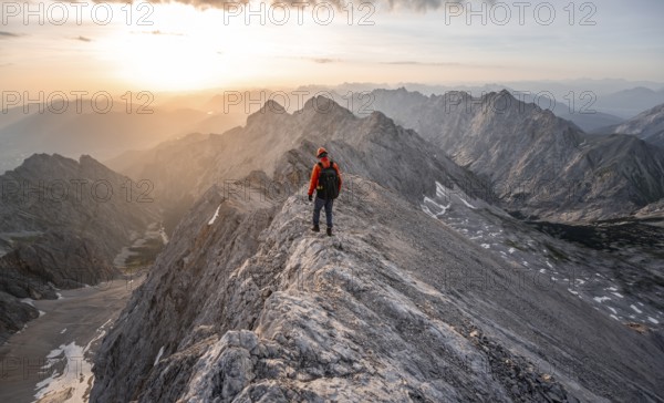 Mountaineer with helmet on a narrow rocky ridge at sunrise, crossing the Jubiläumsgrat, view of Höllental with Höllentalferner and Alpspitze, Wetterstein range, Bavaria, Germany, Europe