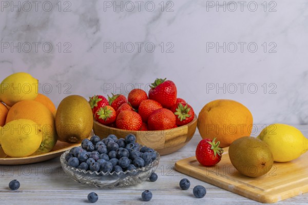 Harmonious still life of various fruits, strawberries, lemons, oranges, kiwis and blueberries on wood against a marble background