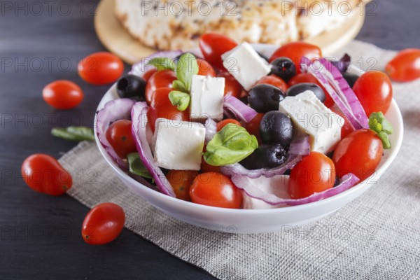 Greek salad with fresh cherry tomatoes, feta cheese, black olives, basil and onion on black wooden background, pancake, close up