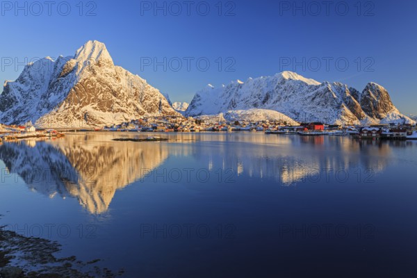 Snow-covered mountains reflected in fjord at sunrise, village, winter, Reine, Moskenesoya, Lofoten, Norway, Europe