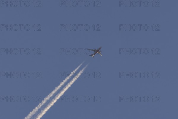 Boeing 787-8 Dreamliner aircraft flying across a blue sky with a vapour trail or contrail behind, England, United Kingdom, Europe