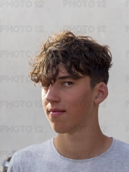 Portrait of a young athletic man with curly brown hair in front of a grey wall, looking into the camera