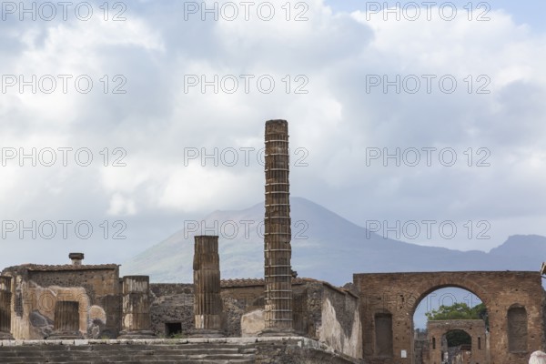 Old stone columns supported by braces and terracotta brick wall building structures plus view of Mount Vesuvius in the background at the ancient ruins of Pompeii in late summer, Campania region, Italy, Europe