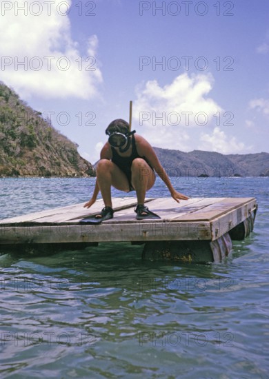 Woman wearing swimwear with snorkel and mask crouching on diving platform oil the sea, island of Tobago, 1963