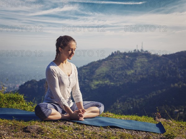 Sporty fit woman practices yoga asana Baddha Konasana, bound angle pose outdoors in HImalayas mountains in the morning with sky. Himachal Pradesh, India. Vintage retro effect filtered hipster style image