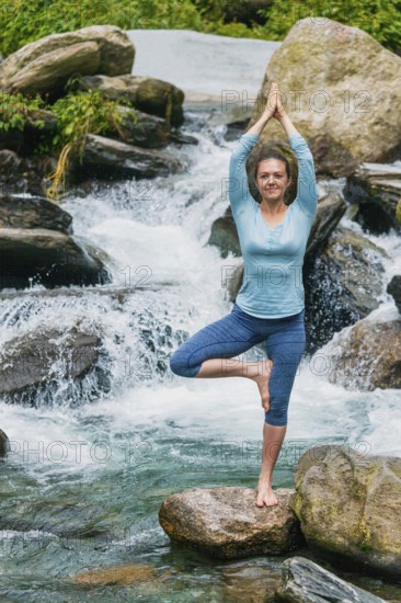 Woman in Hatha yoga balance yoga asana Vrikshasana tree pose at waterfall outdoors