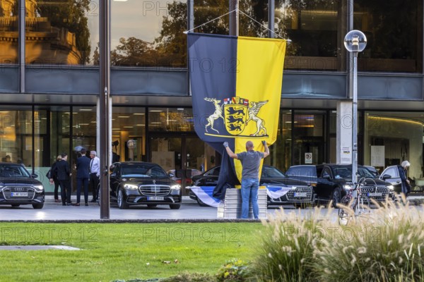 Flag with state coat of arms at the state parliament building, flag is taken down, behind it ministers' official cars, Stuttgart, Baden-Württemberg, Germany, Europe