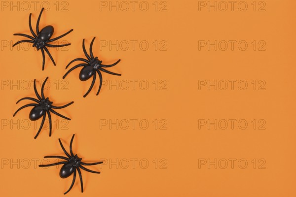 Plastic spiders on side of bright orange Halloween background with empty copy space