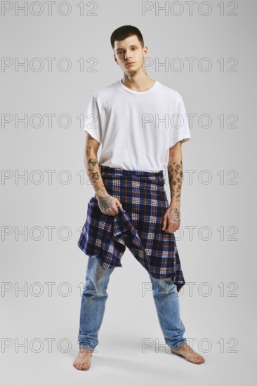 Young cocky man in t-shirt, jeans and checkered shirt tied at the waist