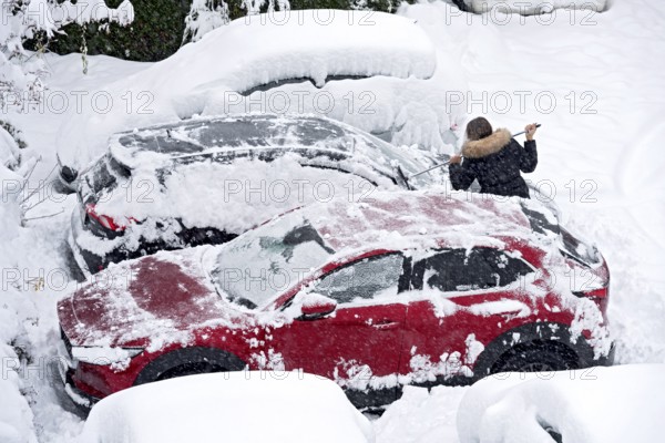 Woman removes fresh snow from car with broom, car, snowed in, heavy snowfall, snow masses, snow chaos, onset of winter, Marzling, Freising, Upper Bavaria, Bavaria, Germany, Europe