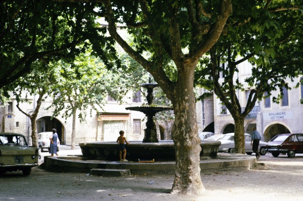 Little boy playing at the fountain in the shade of the trees in the city centre of Uzès, France, 1975, Europe