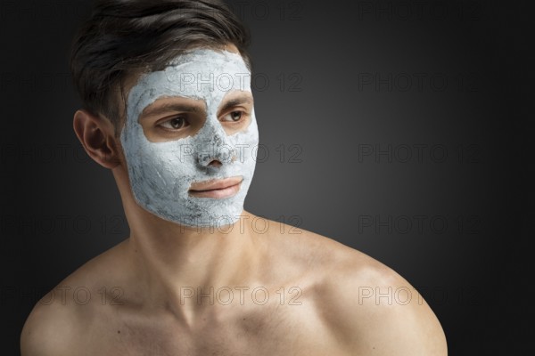 Portrait of a beautiful, relaxed young man with a face mask made of clay, skin care for face and body