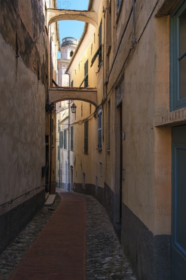 Picturesque narrow alley in the historic town centre with a view of the tower of the baroque church of San Nicola di Bari in the northern Italian municipality of Diano Castello, province of Imperia, Liguria, Italy, Europe