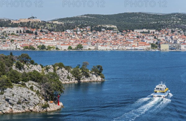 A boat moves through the blue water with a view of a built-up coastal landscape, St Anthony's Channel, Šibenik, Sibenik, Dalmatia, Croatia, Europe