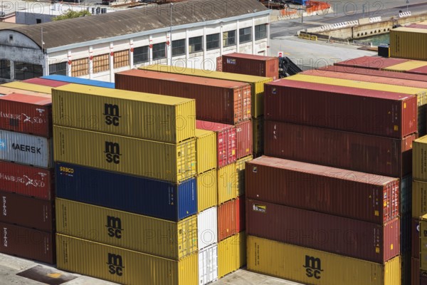 Stacked rectangular metal box shipping containers and warehouse building on dock in La Spezia cargo Port, Italy, Europe