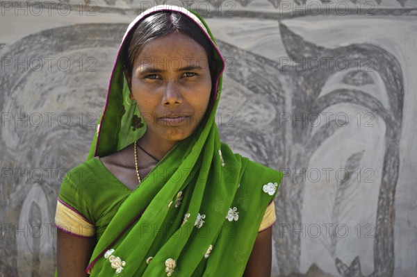 Portrait of a hindu woman. Khovar art in the background. Hazaribagh district, Jharkhand, India. The Khovar (and Sohraï) art are art forms practised by the rural low caste and tribal women in the Hazaribagh district. Every october-november, they paint their house mud walls to welcome the harvest and celebrate the cattle. These paintings depict animals and plants of the surroundiings in a simple way