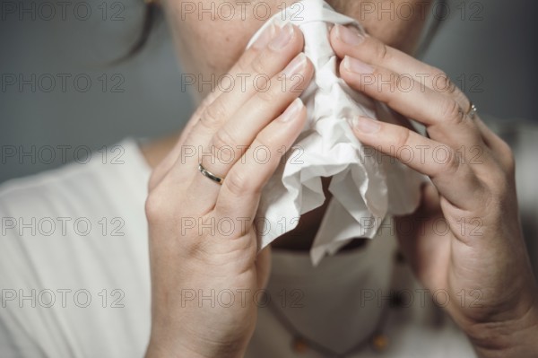 Woman holding a crumpled handkerchief to her nose, possibly with a cold or sneezing, 'symbolic image' cold