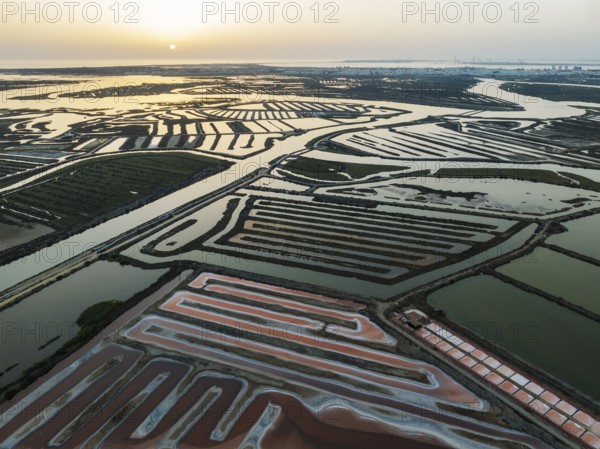 Saline ponds at the salt works near Chiclana de la Frontera. The orange-red colour depends on the level of salinity and is directly caused by the algae Dunaliella salina and brine shrimp. At sunset. Aerial view. Drone shot. Bahía de Cádiz Nature Reserve, Cádiz province, Andalusia, Spain, Europe