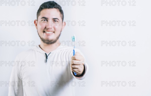 Young man holding toothbrush and looking at camera isolated. Oral health concept