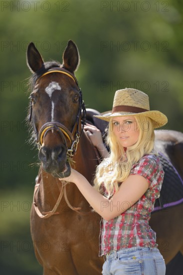 Woman (cowgirl) in a straw hat and plaid shirt stands beside a polish arabian horse on a field, Bavaria