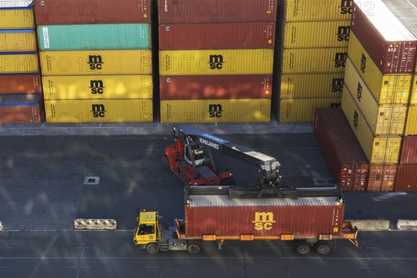 Kone Cranes container handler loading rectangular metal box shipping container onto transportation truck in La Spezia cargo Port, Italy, Europe