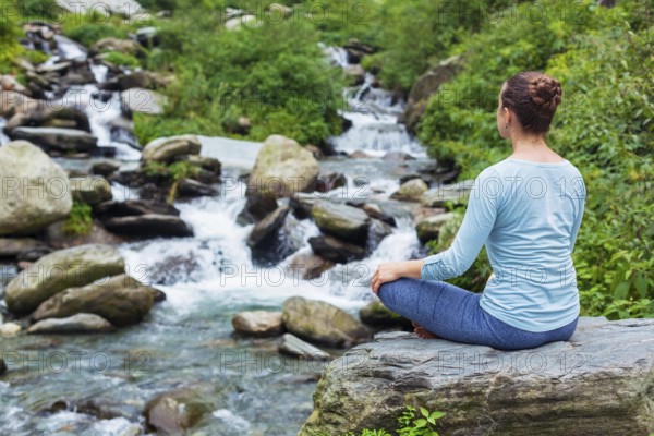 Woman doing yoga meditation asana Padmasana lotus pose outdoors at tropical waterfall