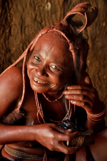 Traditionally dressed Himba woman in her hut, applying perfume, Purros Traditional Village, Purros, Kaokoland, Kunene, Namibia, Africa