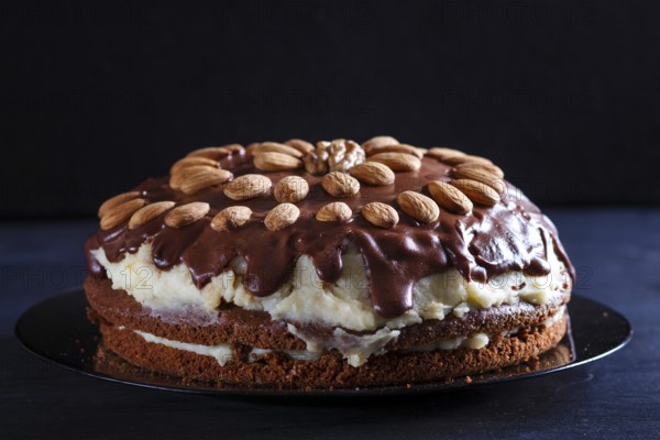 Homemade chocolate cake with milk cream and almonds on black wooden background. close up