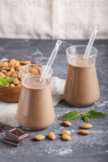 Organic non dairy almond chocolate milk in glass and wooden plate with almond nuts on a black concrete background. Vegan healthy food concept, close up, side view