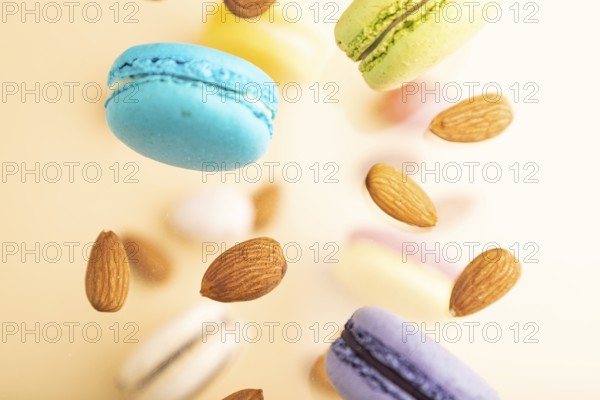 Multicolored flying macaroons and almonds frozen in the air on blurred beige background. top view, flat lay, close up. Breakfast, morning, concept