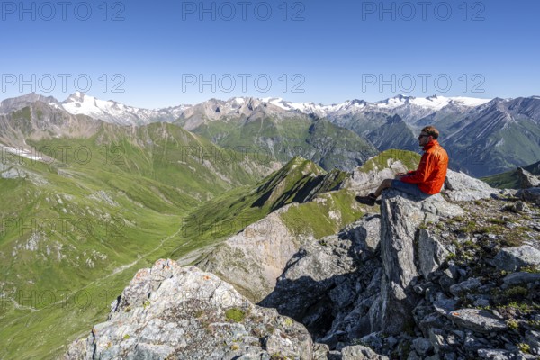 Mountaineer sitting on a rock in front of a mountain panorama with Großvenediger, mountain landscape with mountain peaks of the Venediger group, view from the summit of the Gösleswand, Lasörling group, Hohe Tauern National Park, East Tyrol, Tyrol, Austria, Europe