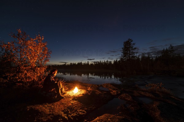 Man in the evening at a bivouac with campfire, Lapland, Sweden, Scandinavia, Europe