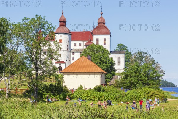 Läckö castle a famous Swedish baroque castle with people sunbathing at the bathing place on a sunny summer day, Läckö, Lidköping, Sweden, Europe