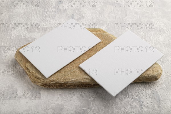 White paper business card, mockup with natural stone on gray concrete background. Blank, side view, still life, copy space, canvas