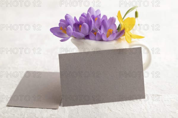 Gray paper business card mockup with spring snowdrop crocus and galanthus flowers on gray concrete background. Blank, business card, side view, copy space, still life. spring concept