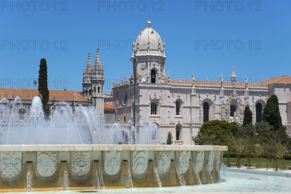 Eine gotische Kathedrale mit imposanten Türmen und einem verzierten Brunnen davor, unter einem klaren blauen Himmel, Hieronymus Kloster, Mosteiro dos Jerónimos, Hieronymitenkloster, Weltkulturerbe, Klosterkirche Santa Maria, Belém, Belem, Bethlehem, Lissabon, Lisboa, Portugal, Europe